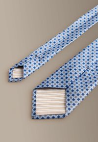 Blåt mønstret slips med diamantformer i rød og marineblå, med en kontrasterende stribet inderside. Glat satinlignende stof, spidse ender.