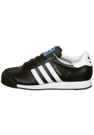 Czarny sneaker Adidas Samoa z białymi paskami, niebieskim logo na języku i białym paskiem na pięcie, widok z boku.