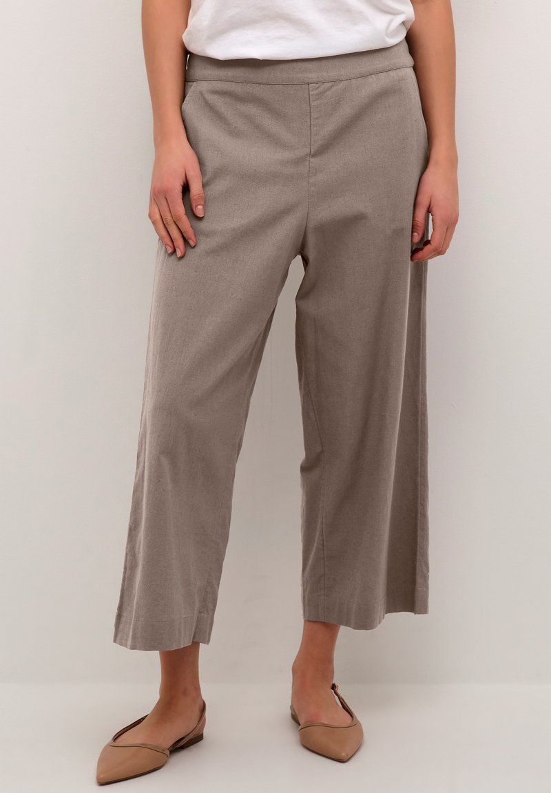 Pantalons courts beige clair avec une texture lisse, une taille élastique et une coupe large. Associés à des ballerines pointues dans une couleur coordonnée.