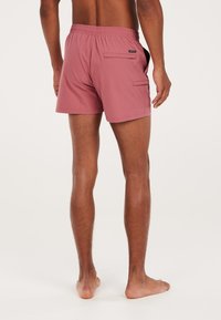 Červené plážové šortky vyrobené z ľahkého materiálu, s elastickým pásom, zadnou vreckom a voľným strihom nad kolenami.