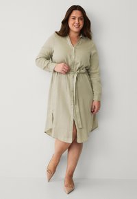 Abito camicia verde chiaro con cintura a fusciacca, maniche lunghe, fessure laterali e vestibilità comoda, realizzato in un tessuto testurizzato.