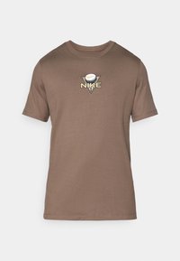T-shirt en coton marron avec un col rond, des manches courtes et un logo en triangle représentant une balle de golf avec le texte "NIKE" brodé en doré.
