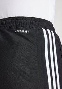 Sorte athletic shorts lavet af letvægtsmateriale, med elastisk talje og tre hvide lodrette striber på hver side. "AEROREADY" logo er vist.