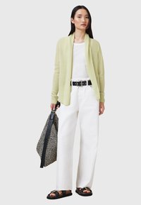Cardigan aperto verde chiaro indossato sopra una t-shirt bianca, abbinato a jeans bianchi a gamba larga e sandali neri. Cintura nera e borsa con motivo inclusa.
