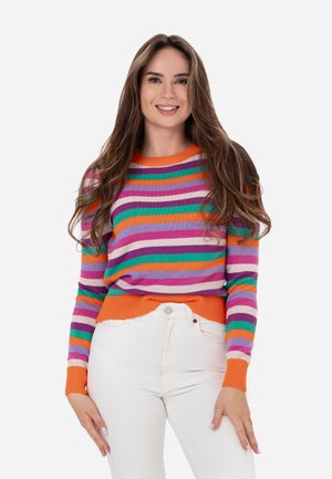 Multicolore gestreepte trui met paarse, oranje, groene en roze strepen. Ribbelmanchetten en -zoom in oranje. Draagt een witte broek.