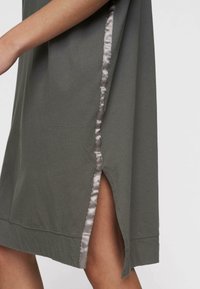 Lekka oliwkowa sukienka z satynowym wykończeniem wzdłuż szwu bocznego i skromnym rozcięciem z boku, charakteryzująca się luźnym krojem i miękką teksturą.