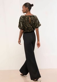 Mustad laiad püksid, millest on kokku pandud lühikesed leopardimustriga ülemised riided, mis sisaldavad võtmekaela tagadetaile ja pehmet, tekstureeritud kangast.