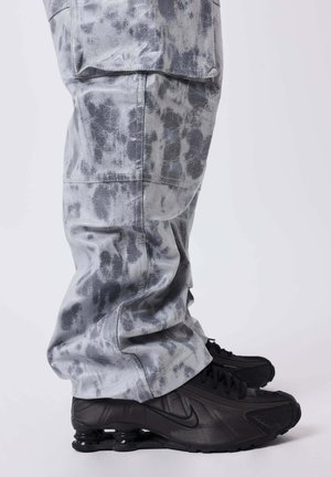 Pantalons gris à motifs avec une texture lisse, dotés d'une coupe décontractée et de poches, associés à des baskets Nike noires avec une semelle distinctive.