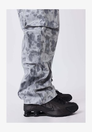 Grijs gemusterde broek met een gladde tekstuur, met een losse pasvorm en zakken, gecombineerd met zwarte Nike sneakers met een kenmerkende zool.