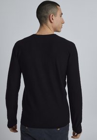 Zwarte langmouwen pullover trui met een ronde hals, lichtgewicht textuur en een aansluitend design. De achterkant toont een gladde stof en minimale details.
