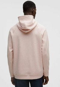 Sudadera de color rosa claro con un cuello alto y capucha con cordón. Presenta una tela texturizada, bolsillos laterales y puños y dobladillo de canalé.