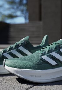 Zelené sportovní boty s texturovaným svrškem, bílým designem tří pruhů a polstrovanou podrážkou označenou "LIGHT BOOST".