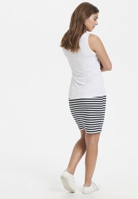 Vit ärmlös topp som parats med en randig marinblå och vit kjol, med en figurnära design, knä-lång kant och vita sneakers.