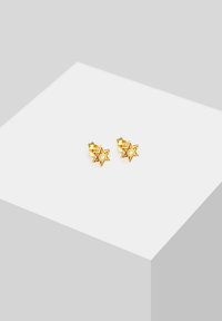 Goldene, sternförmige Ohrringe mit einem zentralen Türkisstein, die kleine Aussparungen entlang der Kanten aufweisen. Glänzende metallische Oberfläche.