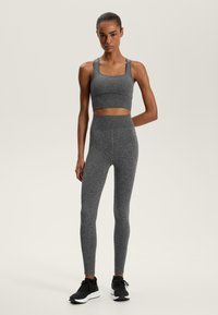 Sutien sport gri și colanți cu talie înaltă dintr-un material texturat. Pantofi sport negri. Design simplu, finisaj fără cusături, siluetă ajustată.