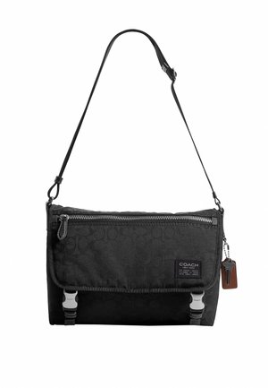 Čierna crossbody taška Coach s nastaviteľným popruhom, predným vreckom na zips, chlopňou s dvoma kovovými zapínaniami a kľúčenkou pripevnenou na boku.