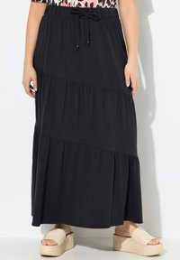 Gonna maxi nera realizzata in tessuto morbido, caratterizzata da strati a balze, una vita elastica con cordoncino e abbinata a sandali con piattaforma intrecciati.