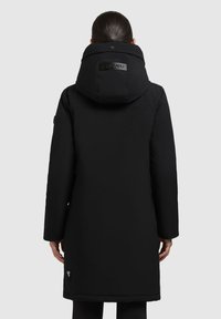 Mustan pikkbullaga pikk parka koos suure kapuutsiga. Omab tekstuuriga kangast, külgseeme taskuid ja logotagi seljal. Ühtlane ja sile viimistlus.