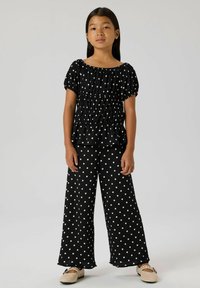 Schwarze Bluse mit Polka-Dots, puffigen Ärmeln und Rüschen an der Taille, kombiniert mit passenden weit geschnittenen Hosen mit Polka-Dots; strukturierter Stoff.