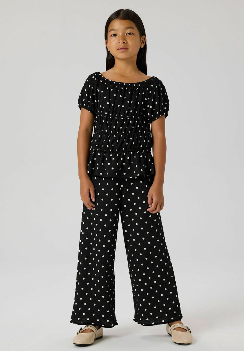 Schwarze Bluse mit Polka-Dots, puffigen Ärmeln und Rüschen an der Taille, kombiniert mit passenden weit geschnittenen Hosen mit Polka-Dots; strukturierter Stoff.