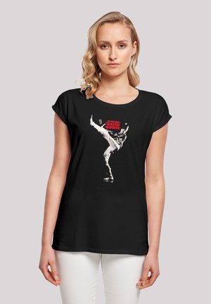 Schwarzes T-Shirt mit Rundhalsausschnitt und umgeschlagenen Ärmeln, das einen grafischen Druck eines Tänzers und "DAVID BOWIE" in fettem roten Text zeigt.