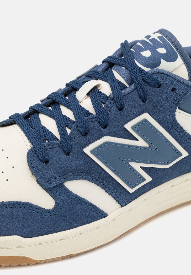 Blaue Wildleder- und Ledersneaker mit weißen Akzenten, dicken Schnürsenkeln und einem auffälligen "N"-Logo an der Seite. Texturierte Oberfläche.