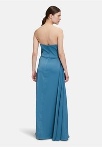 Langes, trägerloses Kleid aus einem weichen Türkisstoff, mit einem taillierten Oberteil und einem fließenden Rock, der hinten mit Drapierung verziert ist. Geschmeidige Textur.