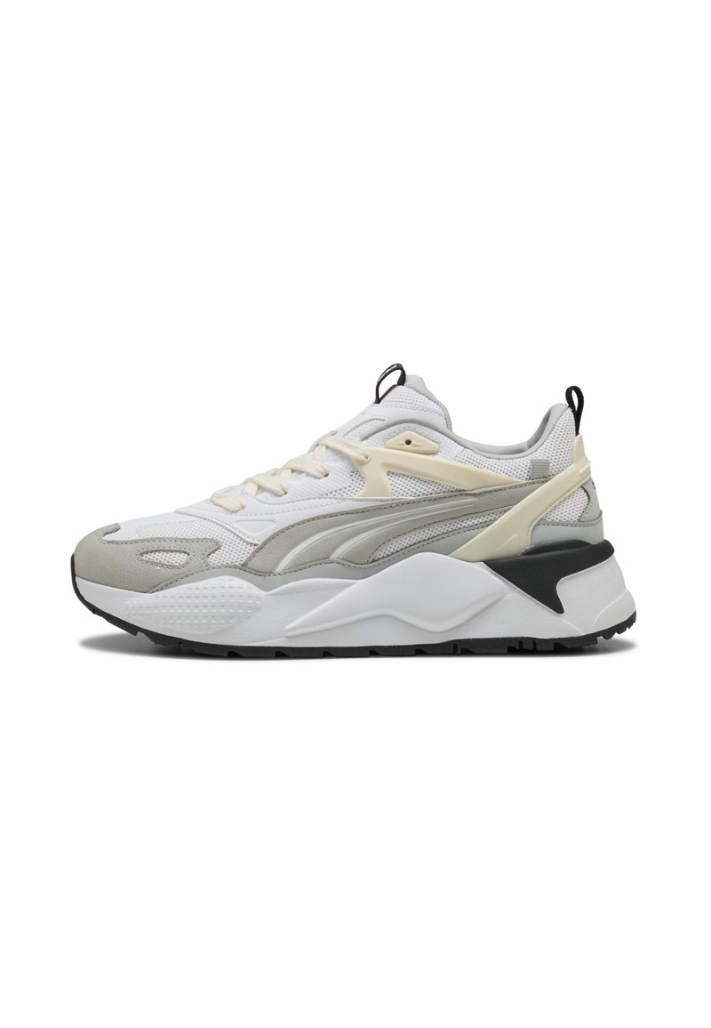 Baskets de sport blanches et grises avec des superpositions beige, des languettes noires, une semelle blanche épaisse et une semelle extérieure texturée montrant le profil latéral de la chaussure.