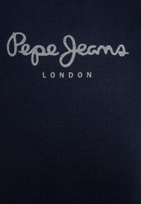 Tamsiai mėlynas medvilninis marškinėlis su sidabro blizgučio tekstu "Pepe Jeans LONDON", kuris yra centruotas krūtinėje, su lygiu audinio tekstūru.