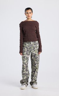 Top de manga larga marrón texturizado con diseño off-shoulder, combinado con pantalones de camuflaje verdes y zapatillas blancas.