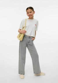 Camiseta blanca corta con diseño de cereza roja, pantalones de mezclilla anchos grises, bolso amarillo de hombro y zapatos beige sin cordones. Tejido suave y contraste de colores destacado.