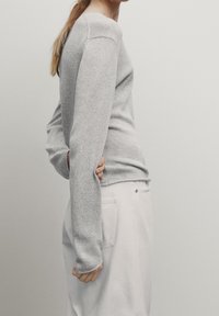 Gray knitted sweater with long sleeves, ribbed cuffs, and a round neckline, paired with light-colored pants. Soft texture and fitted design.