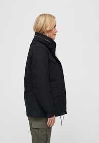 Svart, isolert jakke med høy krage, flere lommer og glidelåsdetaljer. Har en skreddersydd passform og solid stoffstruktur.