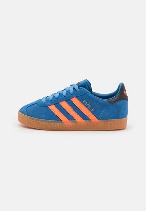 Blå semsket sneakers med oransje striper, med en gummirubber såle og svart hælkrage. Snøringen matcher skoens farge. Modellnavn: Gazelle.