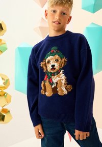 Marineblauer gestrickter Pullover mit einem detaillierten braunen Hund, der einen grünen Hut und einen roten Schal trägt. Weiche Textur, gerippte Ärmelbündchen und Saum.