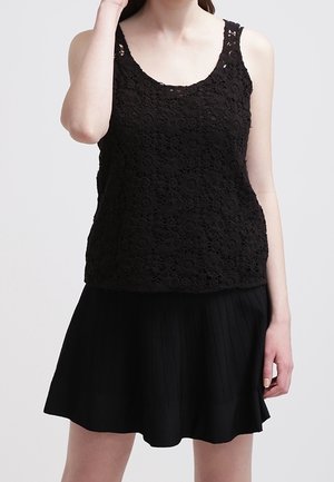 Top sans manches en dentelle noire avec un motif floral complexe, en tissu légèrement texturé, associé à une jupe plissée noire.