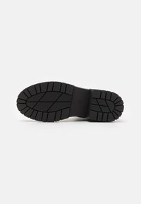 Semelle de chaussure en caoutchouc noir avec des rainures profondes et des motifs pour une meilleure traction. Design plat avec des bords larges et une zone centrale surélevée pour le soutien.