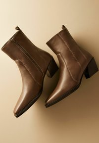 Bottines en cuir marron au design élégant, avec des pointes pointues, des zips latéraux et des talons carrés. Les détails de couture ajoutent de la texture et de la dimension.