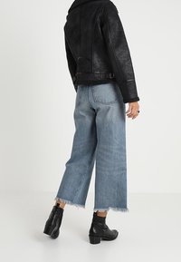 Czarna kurtka z sztucznej skóry z kołnierzem z owczej wełny, w zestawieniu z jasnoniebieskimi dżinsami o szerokich nogawkach z postrzępionymi brzegami i czarnymi botkami do kostki.