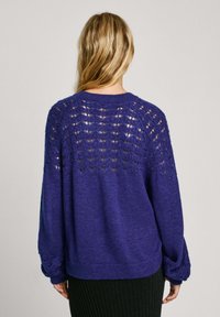 Mörkblå stickad tröja med ett texturerat öppet stickmönster på baksidan, lösa ärmar och ribbstickad kant vid nederkanten.