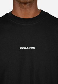 Μαύρη βαμβακερή μπλούζα t-shirt με στρογγυλή λαιμόκοψη και λευκό λογότυπο "PEGADOR" εκτυπωμένο στο στήθος. Μαλακή υφή και κανονική εφαρμογή.