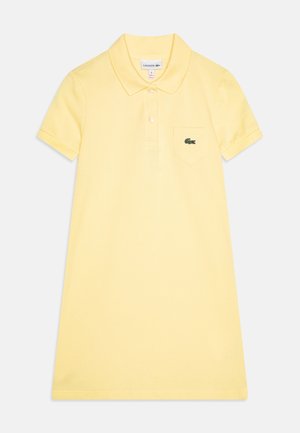 Polo jurk in lichtgele katoen met korte mouwen, een kraag en een borstzak met een groen Lacoste-logo.