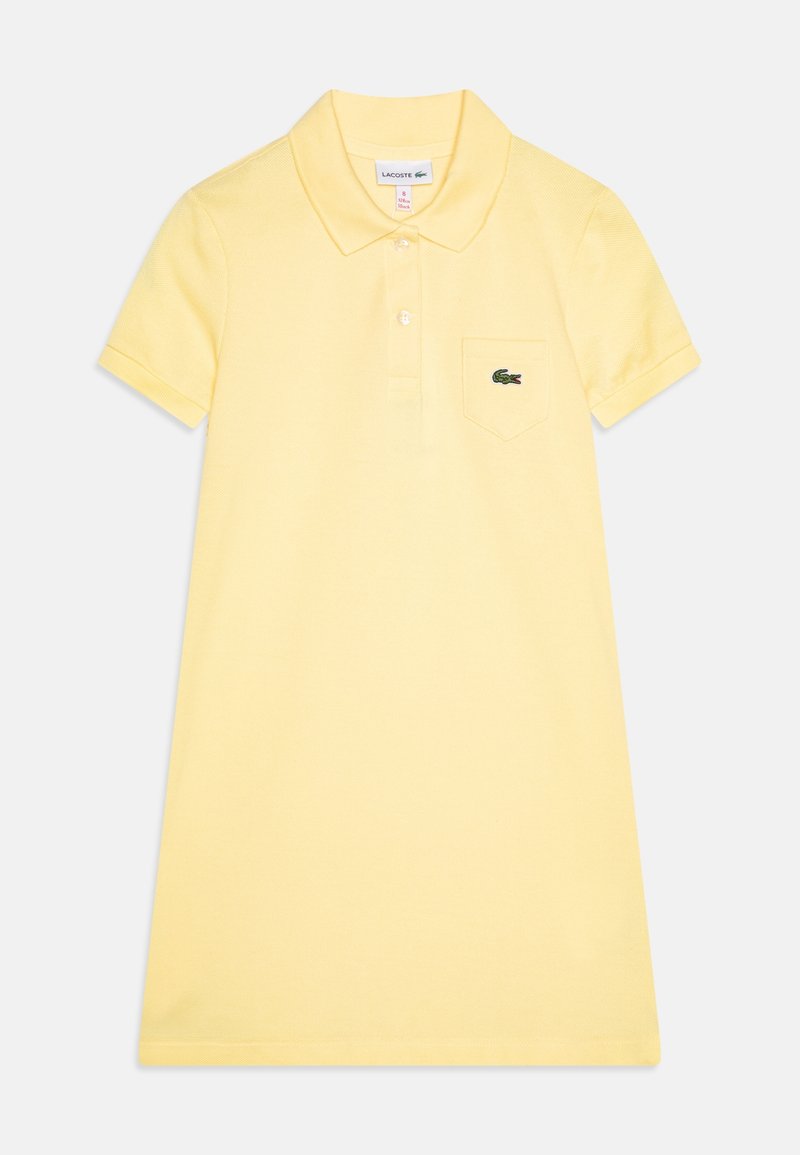 Polodress i ljusgul bomull med korta ärmar, krage och ett bröstfick med en grön Lacoste-logga.