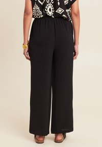 Zwarte, wijde broek met een elastische tailleband, met een gladde textuur en een losse pasvorm, gecombineerd met een gemusterd topje en eenvoudige schoeisel.