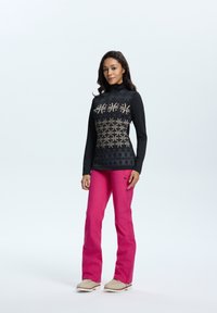 Langemouwen zwart top met een patroon in goud en grijs, gecombineerd met felroze broeken en beige sneeuwlaarzen. Gladde stoftextuur.