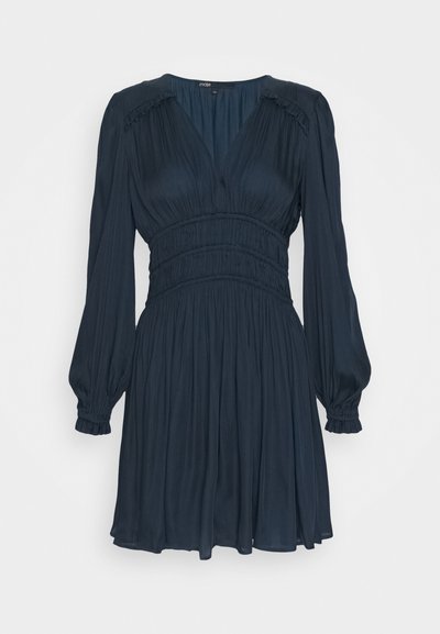 Rochie de culoare bleumarin închis, cu mâneci lungi și pufoase, decolteu în formă de V, talie elastică și fustă fluidă. Fabricată dintr-un material moale, drapat, cu o textură netedă.