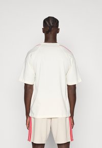 Kremowy t-shirt z krótkim rękawem z czerwonymi akcentami, w połączeniu z jasnobeżowymi szortami z czerwonymi paskami po bokach; wykonany z bawełny, o swobodnym kroju.