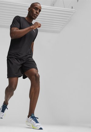 Black athletic t-shirt and shorts, paired with white and navy running shoes featuring green accents, model in a running stance.
