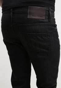 Jeans de mezclilla negra con un acabado texturizado, que cuentan con una etiqueta de cuero con la inscripción "BOSS ORANGE" en la parte trasera de la cinturilla y dos bolsillos traseros.