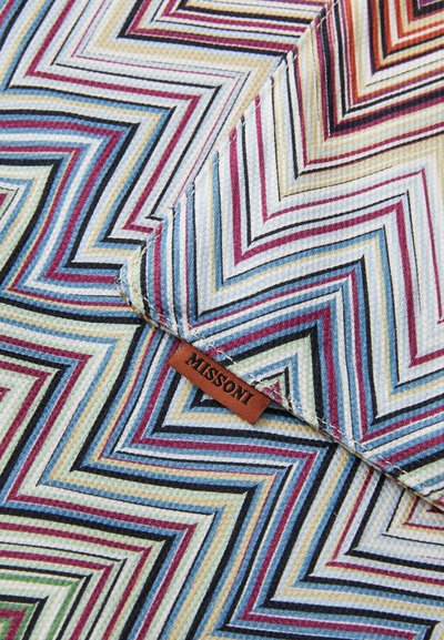 Colorful zigzag patterned fabric in shades of blue, red, yellow, and black, with a brown leather tag labeled "MISSONI." Textured weave design.